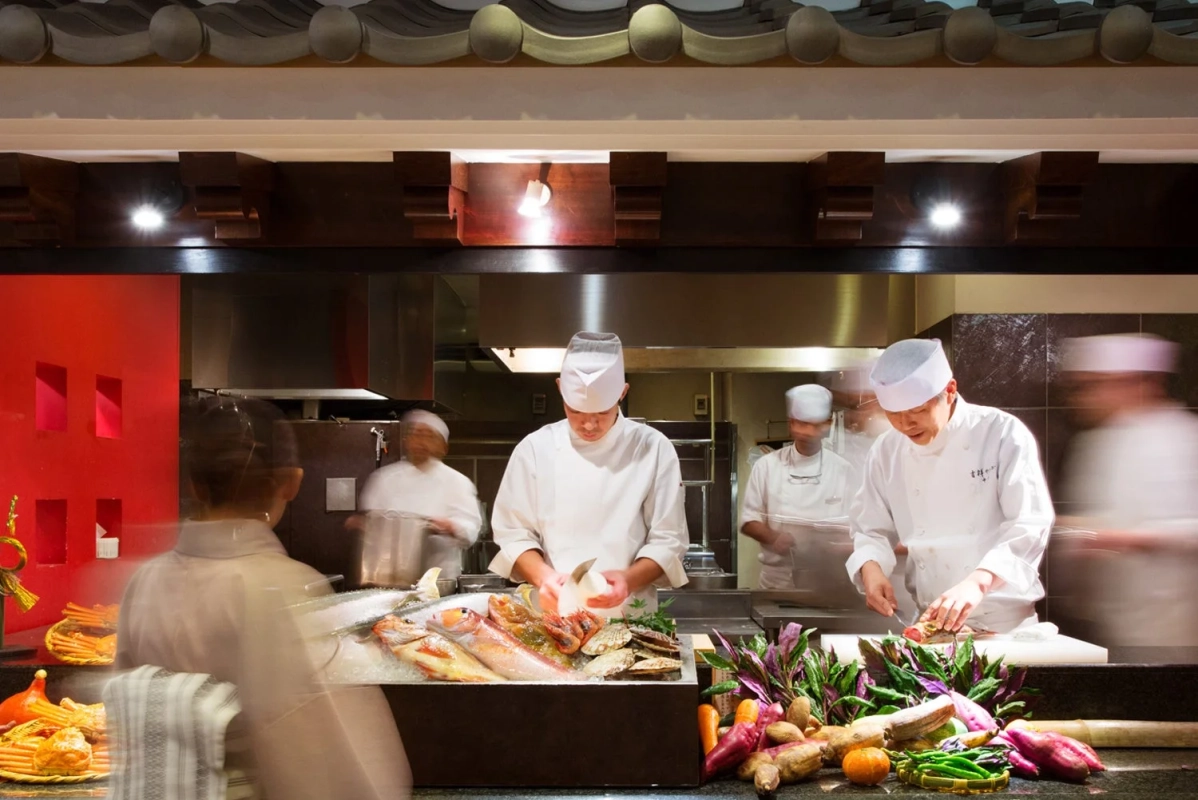 複数の料理人が厨房で新鮮な魚介類や野菜を調理している様子