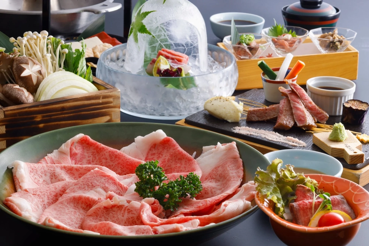 薄切りの和牛や鍋野菜、氷に盛られた刺身、グリルされた肉、小鉢などが並ぶ豪華な和食の会席料理です。彩り豊かで美しい盛り付けが特徴の、特別な食卓の風景です。