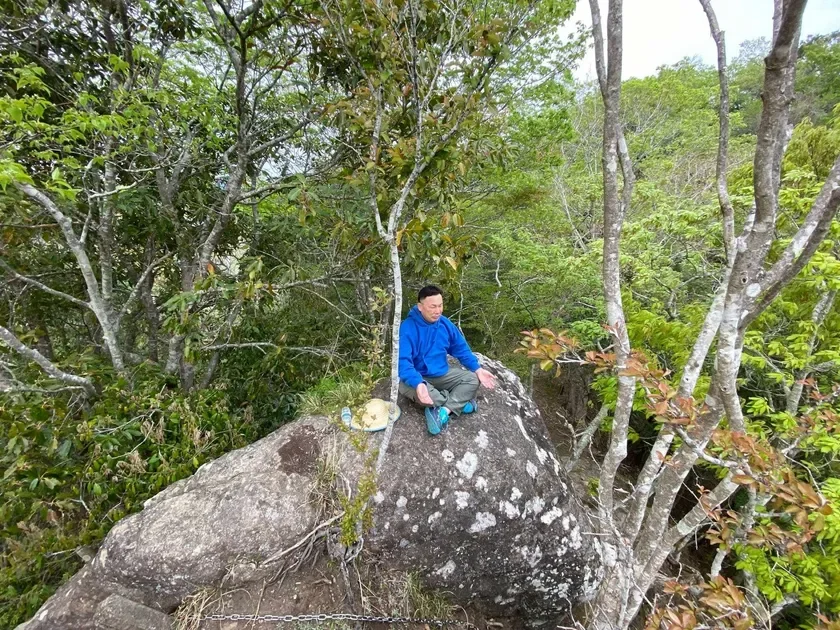 森の中の大きな岩に座ってリラックスする男性