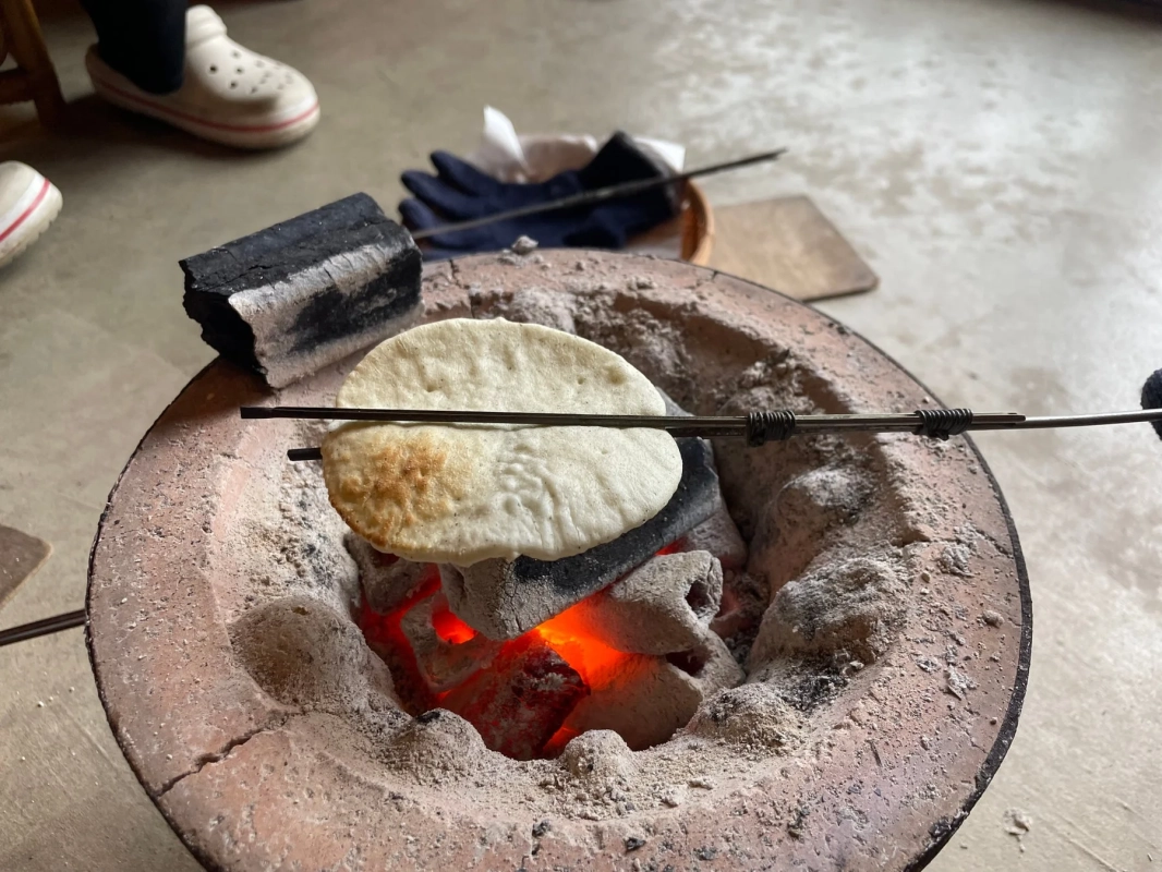 伝統的な囲炉裏で、熱い炭火を使って平たい餅のようなものを焼いている様子