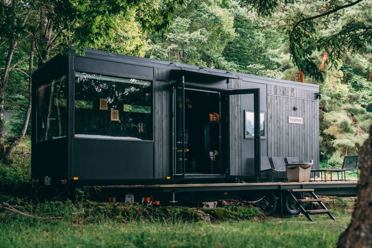 森の中に佇むモダンな黒いトレーラーハウス