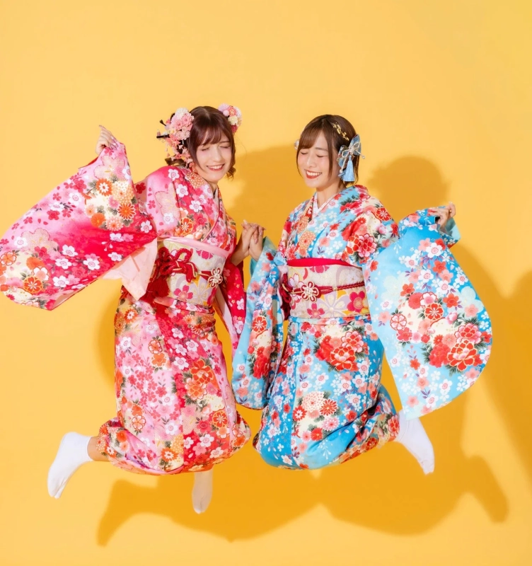 鮮やかな花柄の振袖を着た二人の女性が手をつないで楽しそうにジャンプしている