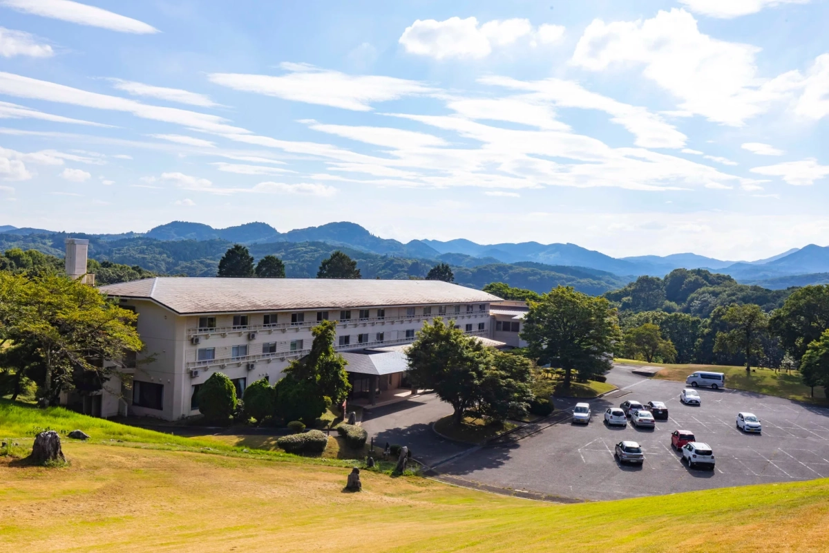 緑の丘陵地に建つ白い建物(ホテルまたはリゾート)と駐車場