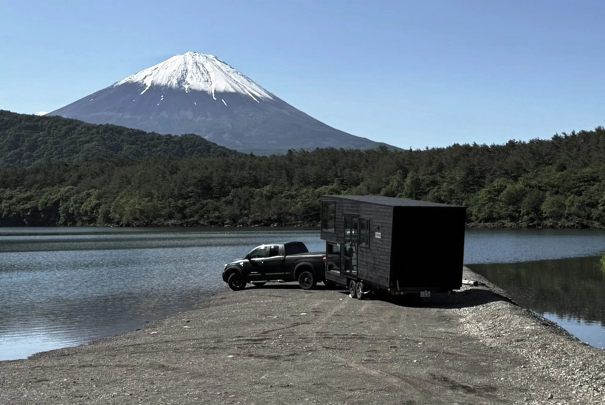 富士山を背景に湖畔に停まる黒いピックアップトラックとタイニーハウス