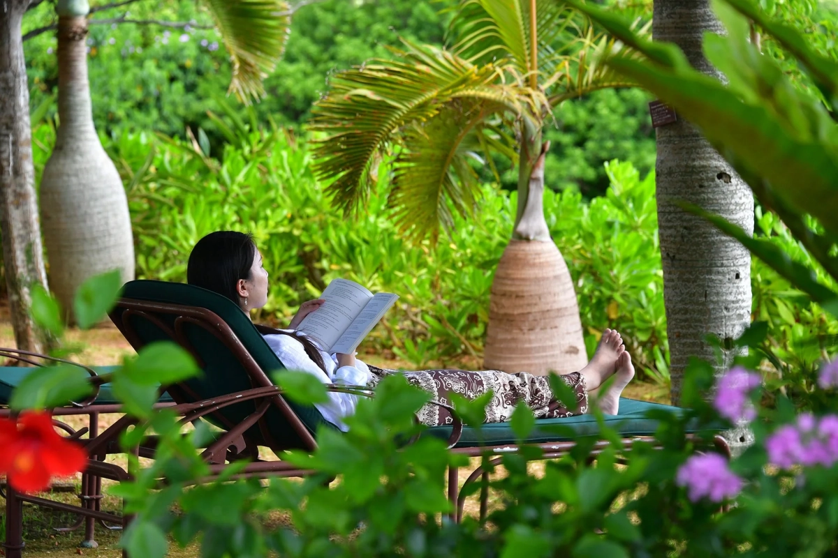 熱帯の庭園で、女性がラウンジチェアに座って本を読んでリラックスしている