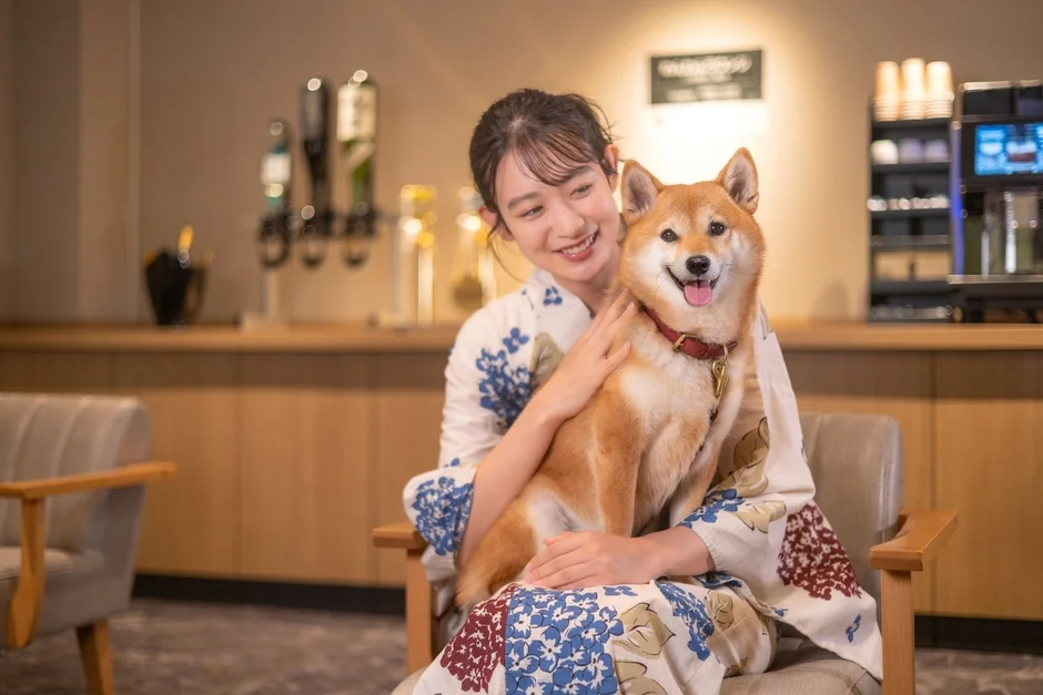 浴衣を着た女性が満面の笑みで柴犬を抱きかかえています。柴犬も舌を出して笑顔のように見え、とても幸せそうな様子です。室内でくつろいだ雰囲気が伝わってきます。