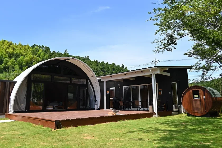 森を背景にしたグランピング施設とバレルサウナ