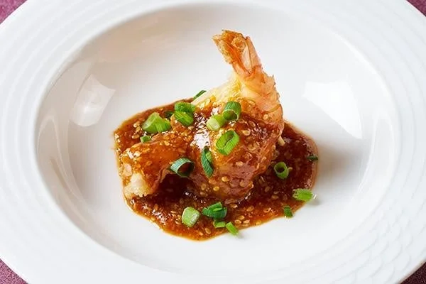 白い皿に盛られた濃厚なごまソースがたっぷりかかった大きなエビの料理