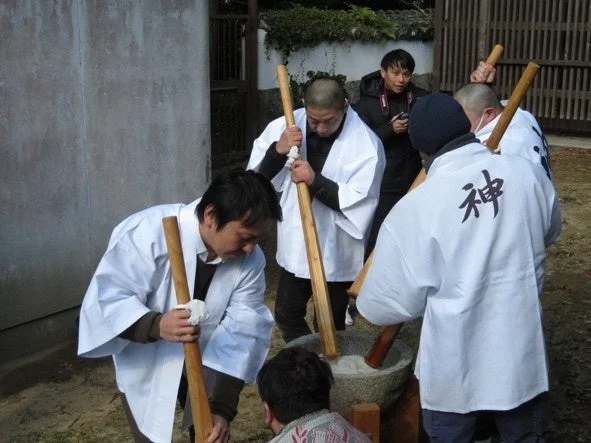 屋外で数人の男性が臼と杵を使って餅つきをしている様子