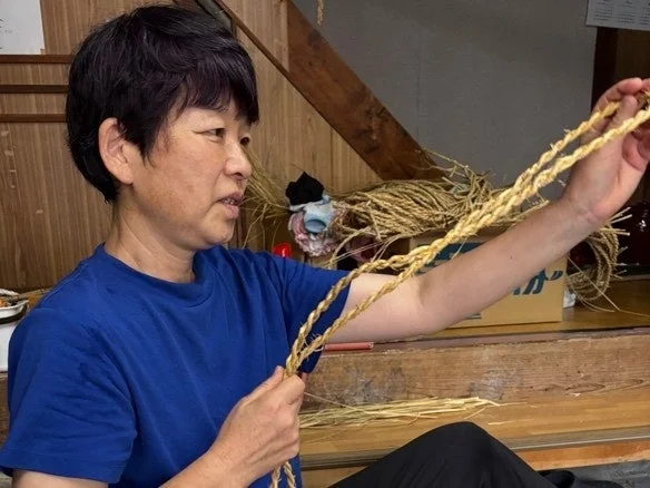 青いTシャツを着た女性が藁のような素材を丁寧に編んで手作業をしている様子