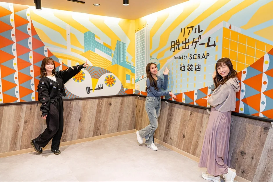リアル脱出ゲーム池袋店のカラフルな壁画の前でポーズをとる3人の女性
