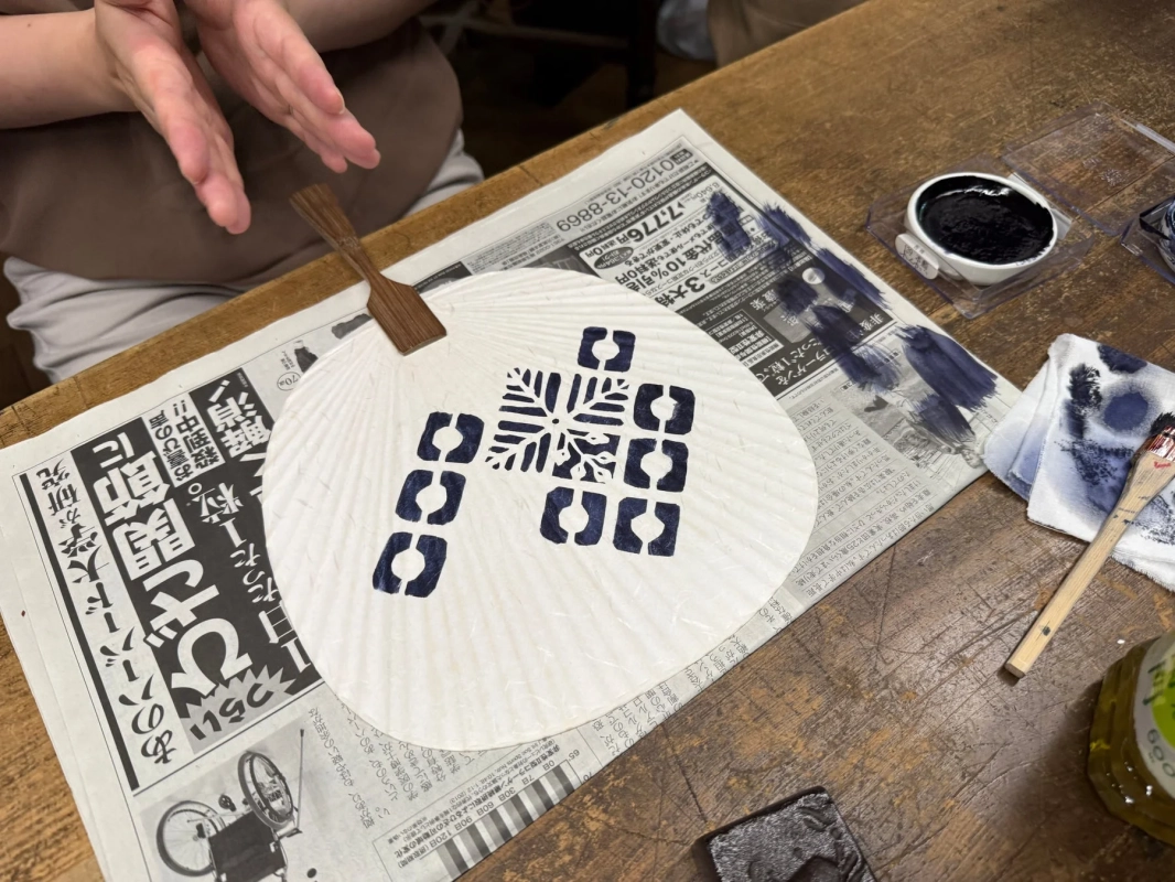 白い団扇に青い染料で伝統的な模様を施している作業風景