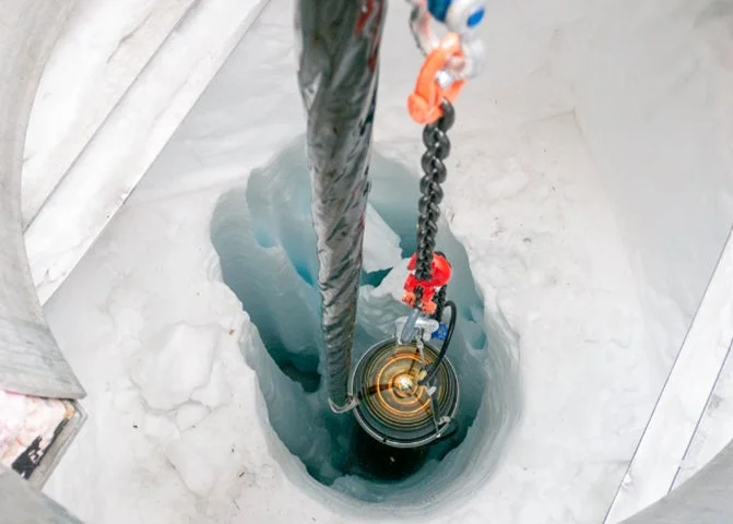 氷河に開けられた深い穴に、発光する科学機器がケーブルで吊り下げられ、調査されている様子。