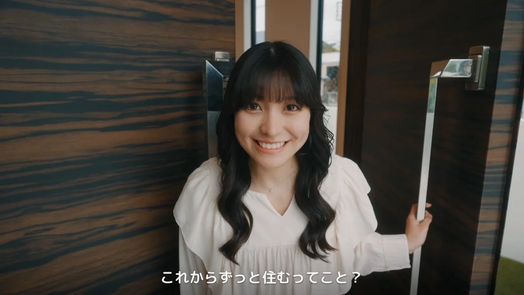 明るく微笑む若い女性が、新しい住居のドアを開けようとしている様子です。