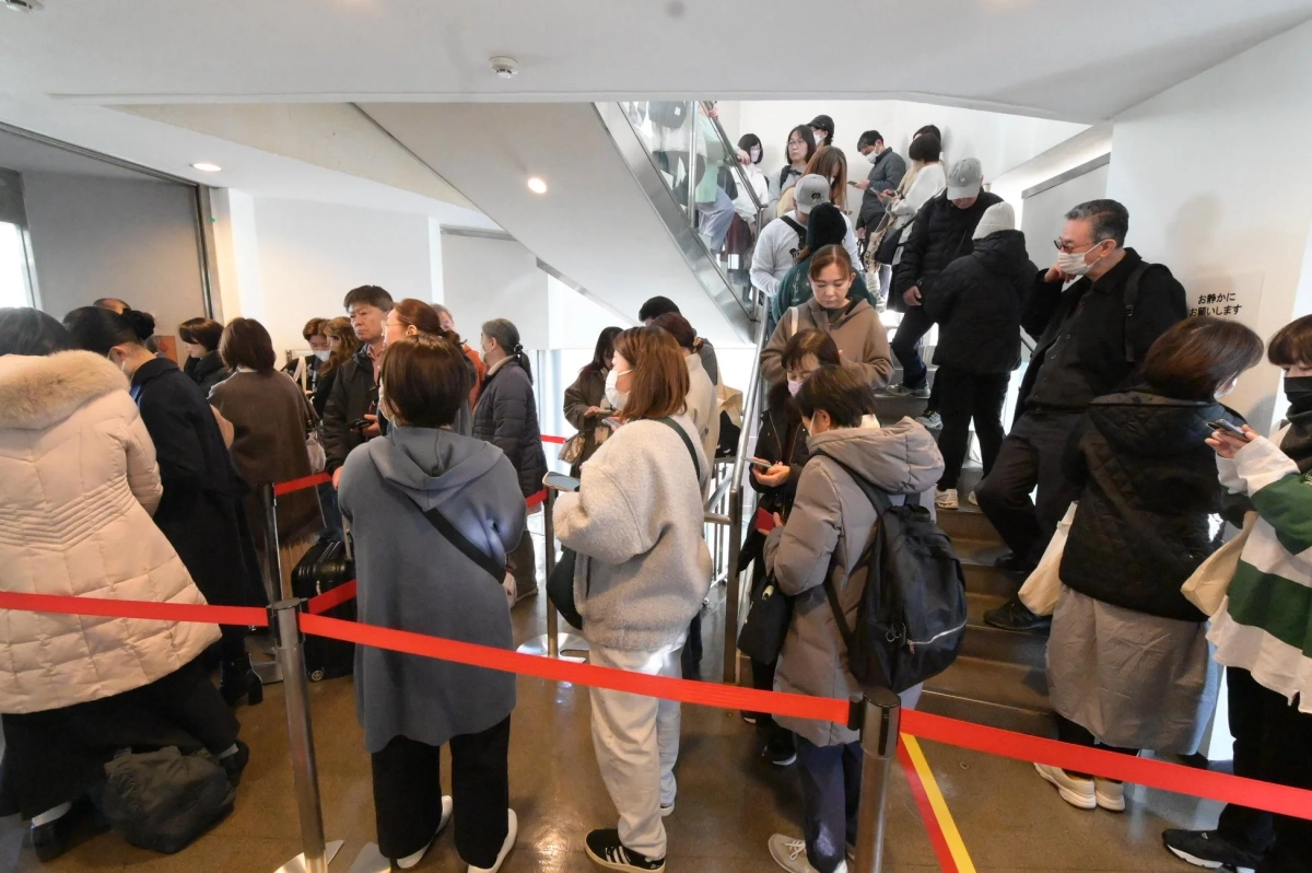 屋内の公共スペースで多くの人々がマスクを着用して列をなして待っている様子