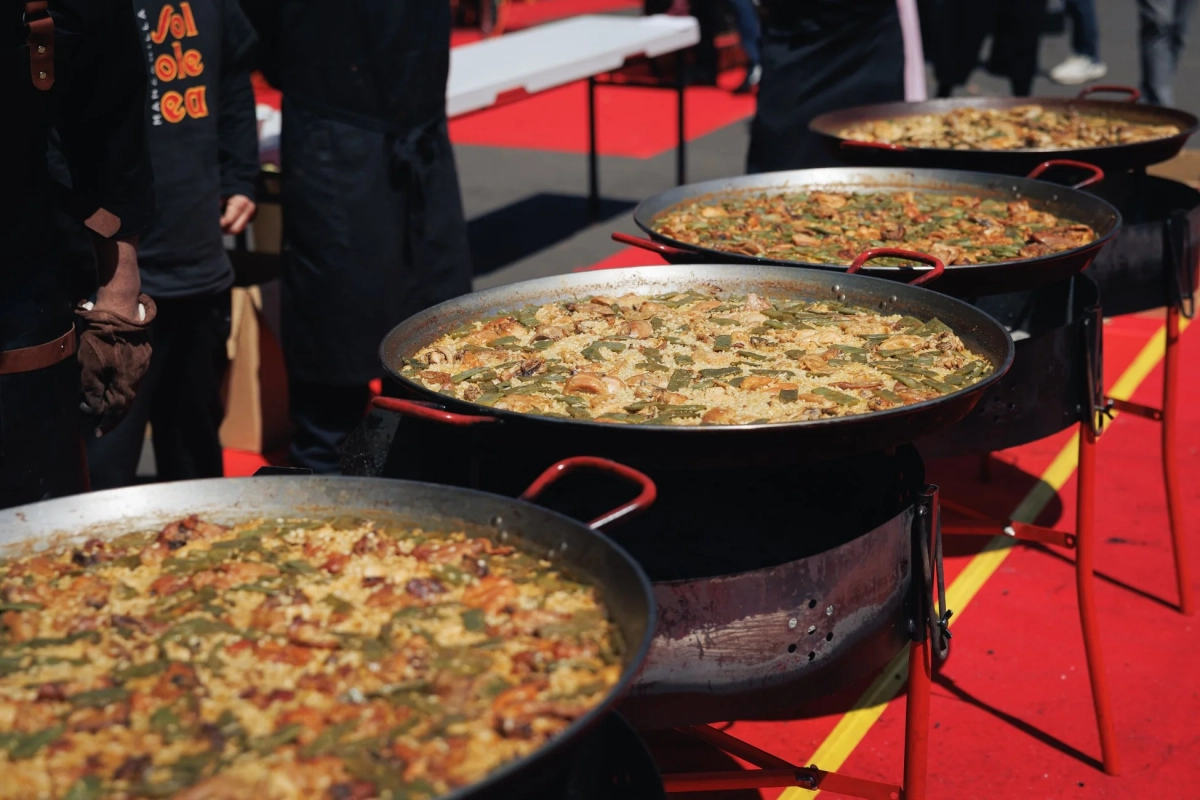 屋外イベントで複数の大きなパエリア鍋が並べられている