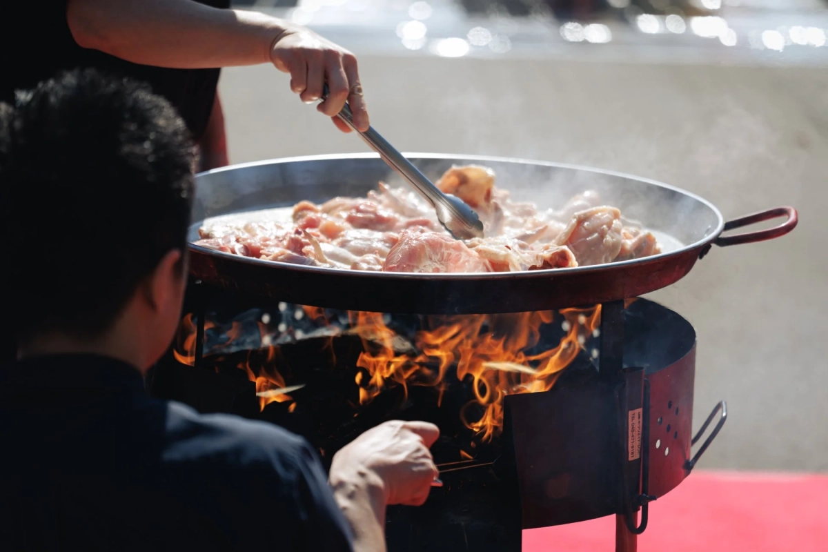 屋外で大きなパエリア鍋で鶏肉を薪火調理する様子