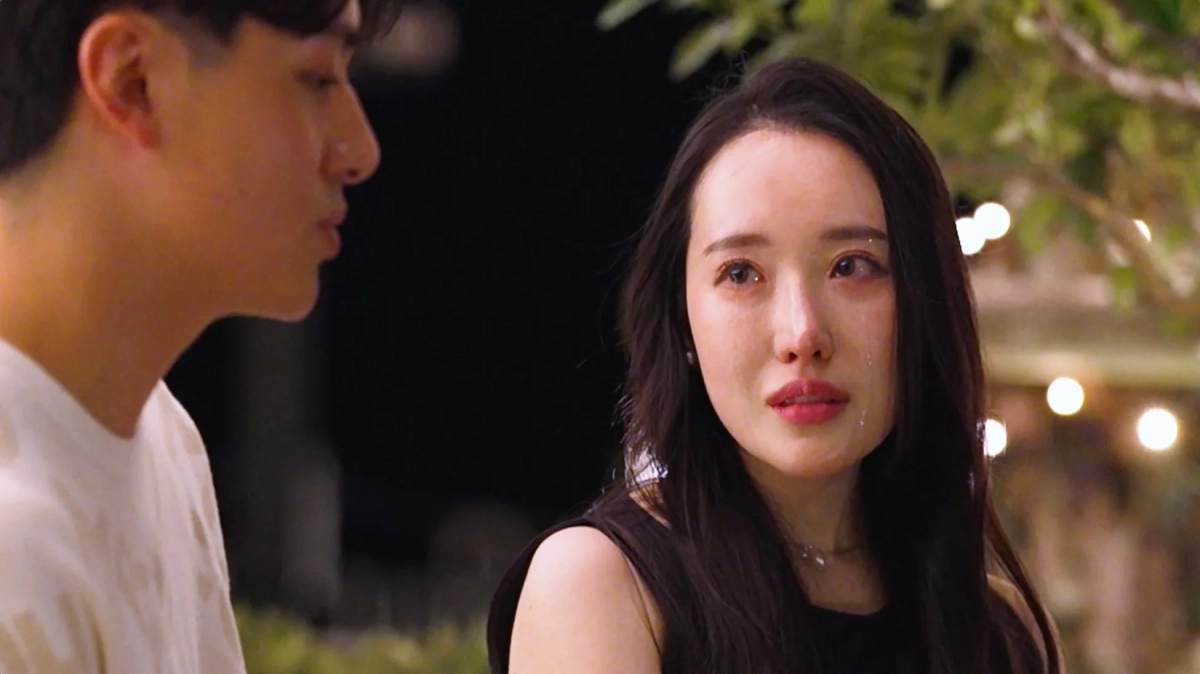 夜の屋外で、涙を流す女性と、その話を聞いているような男性の姿