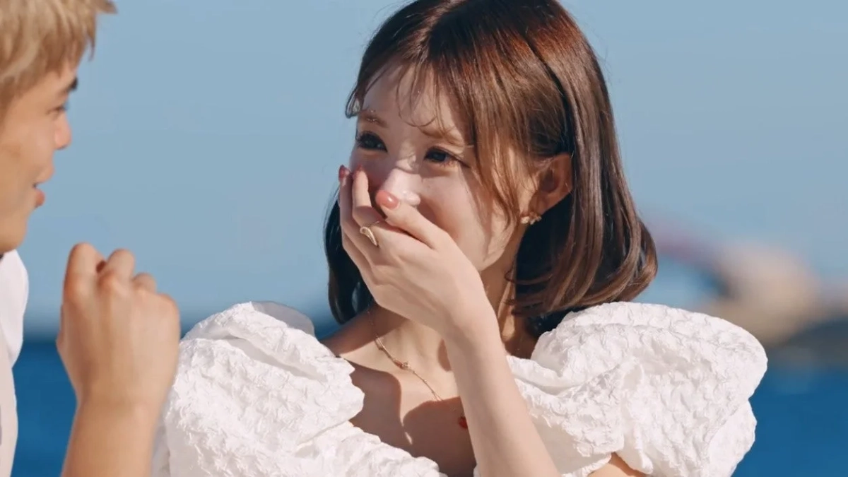 白い服を着た女性が男性の方を見て、手で口元を隠しながら照れたように微笑んでいる