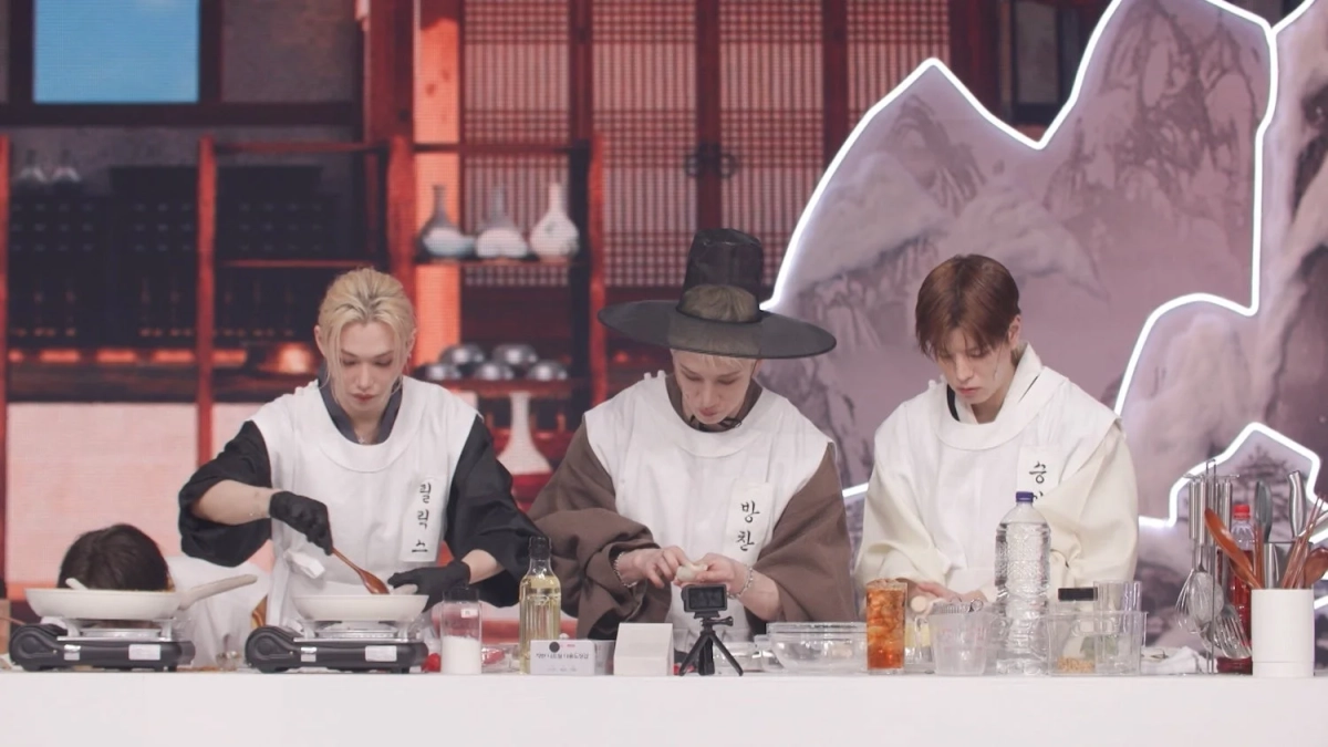 伝統的な衣装を身につけた3人の男性が、調理台で料理をしている様子。