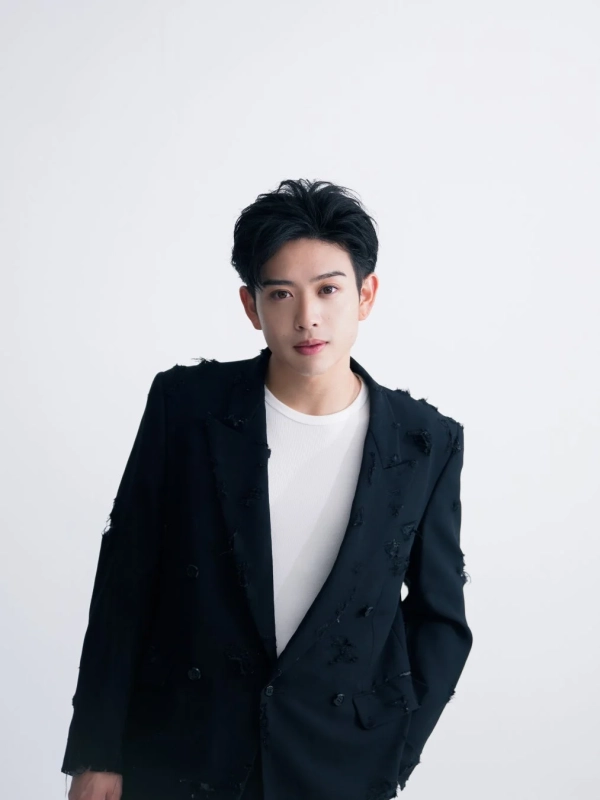 白い背景をバックに、黒いダメージ加工のジャケットと白いTシャツを着用した若い男性がカメラを見つめているポートレート写真です。クールな表情が特徴的です。