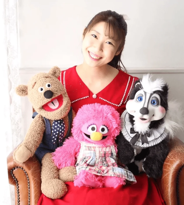 笑顔の女性がパペットに囲まれて座っているポートレート