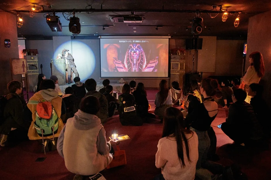 イベント会場でスクリーンとパフォーマーを見る観客たち