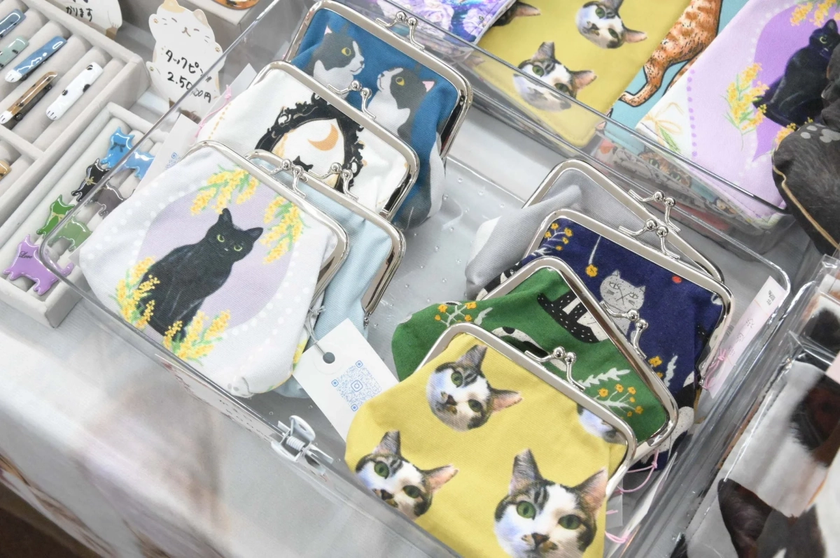 猫のイラストや顔がデザインされたがま口財布や、猫をモチーフにした小物入れなどが透明なケースに多数陳列されている様子