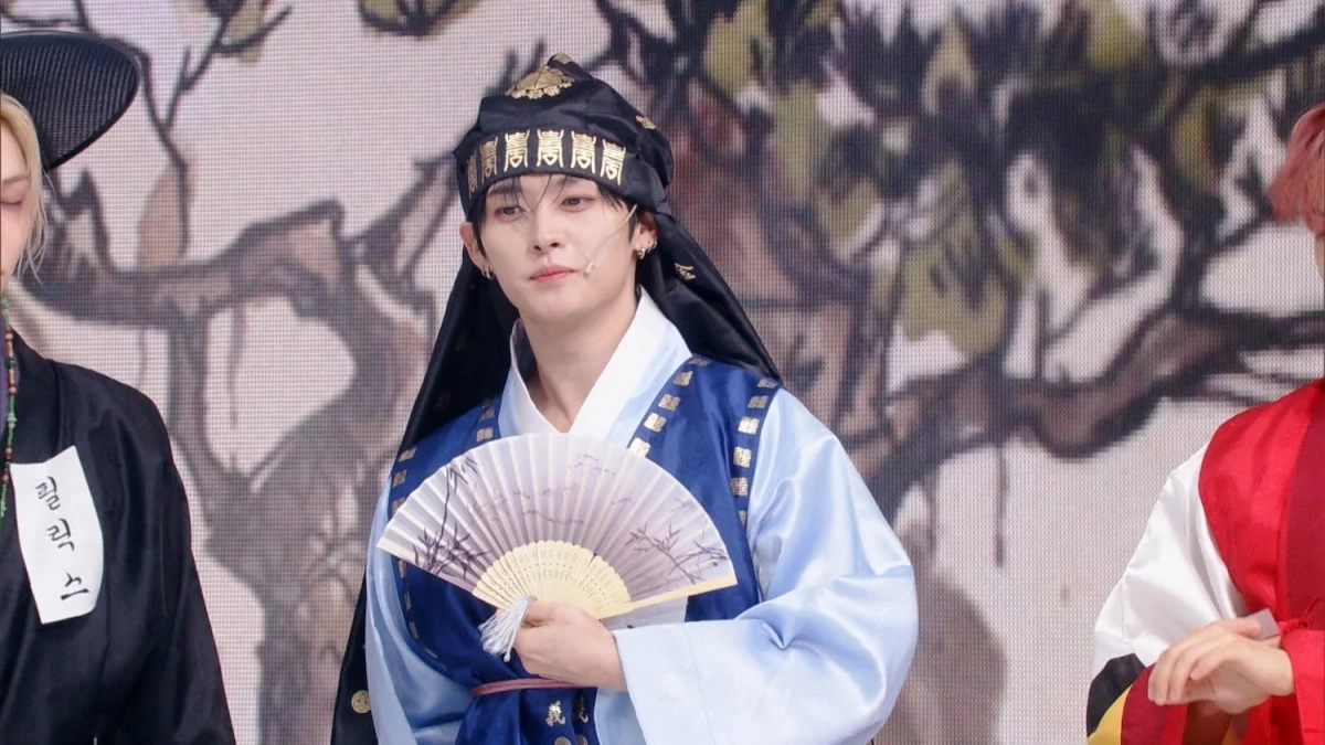 伝統的な韓服を着用し、扇子を持った男性アイドルがステージに立っている様子です。