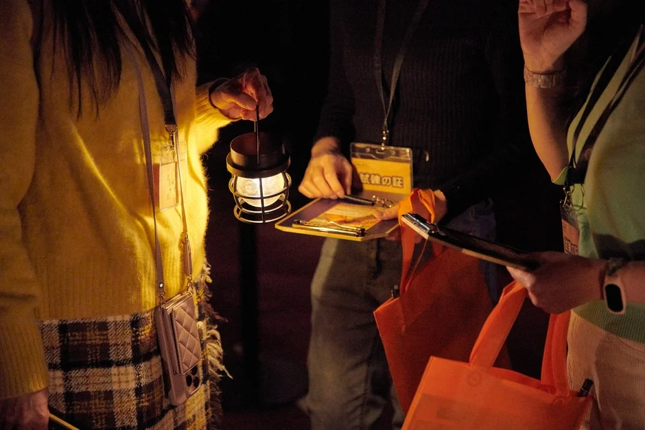 暗い部屋でランタンを手に謎を解く参加者たち