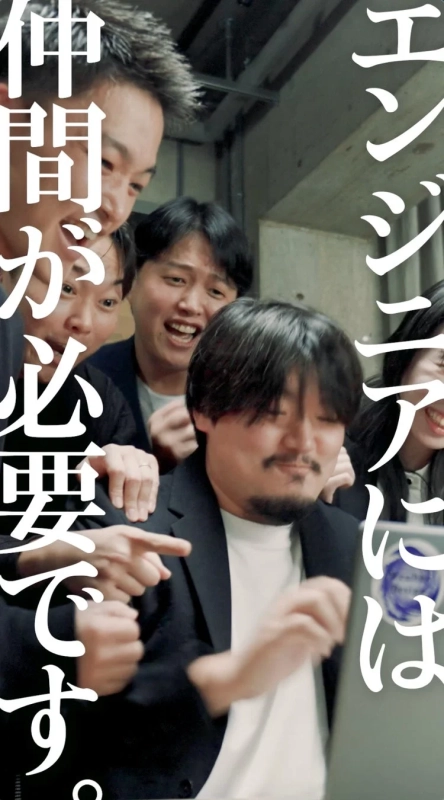 PCを囲んで笑顔で協力し合うエンジニアらしき人々