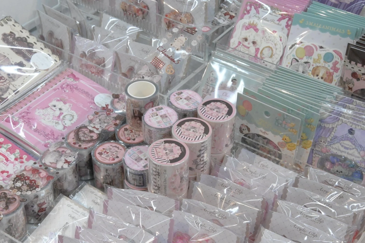 可愛い動物やスイーツのイラストが描かれたマスキングテープ、ノート、シール、アクリルクリップなどのファンシーな文房具が並べられた売り場の様子