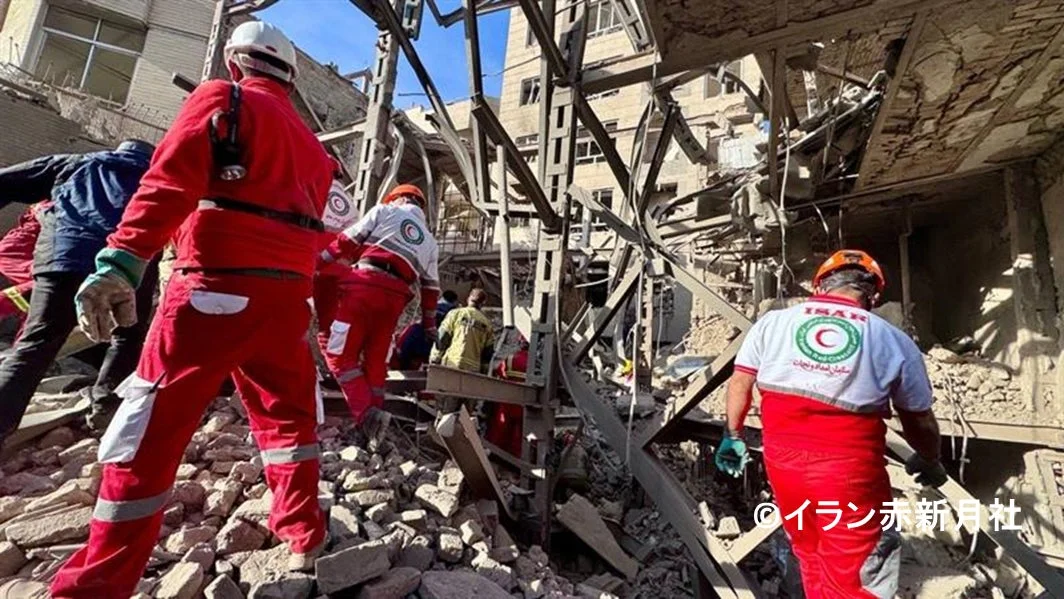 破壊された建物と瓦礫が散乱する災害現場で、赤い制服を着た救助隊員たちが捜索活動を行っている様子