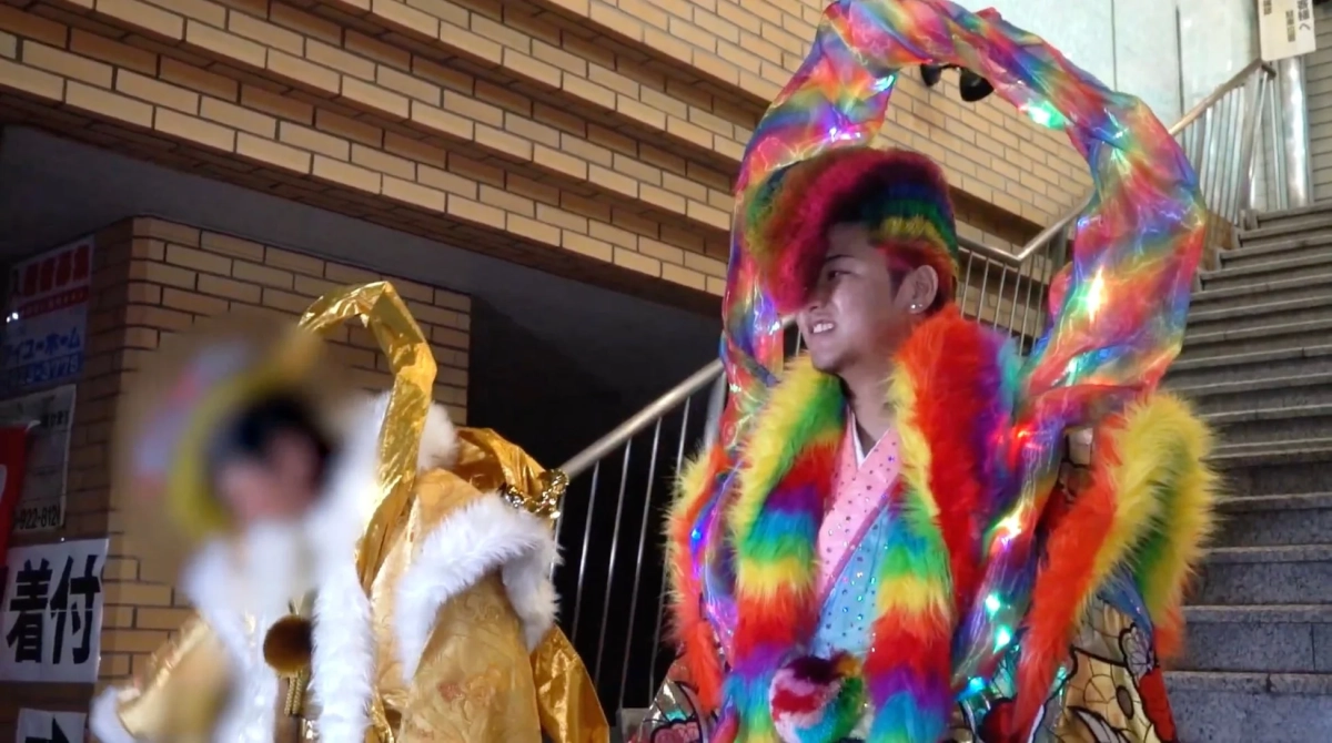 虹色の髪と羽の派手な衣装の人物