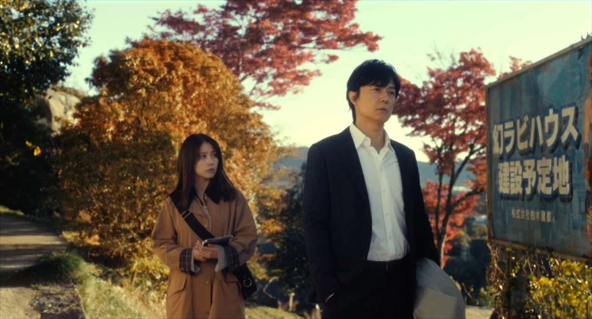 建設予定地の看板の前に立つ男女の画像