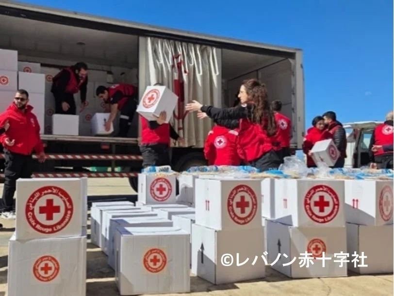レバノン赤十字社のボランティアたちが、赤い十字のマークが付いた支援物資の箱をトラックから運び出し、積み上げている様子