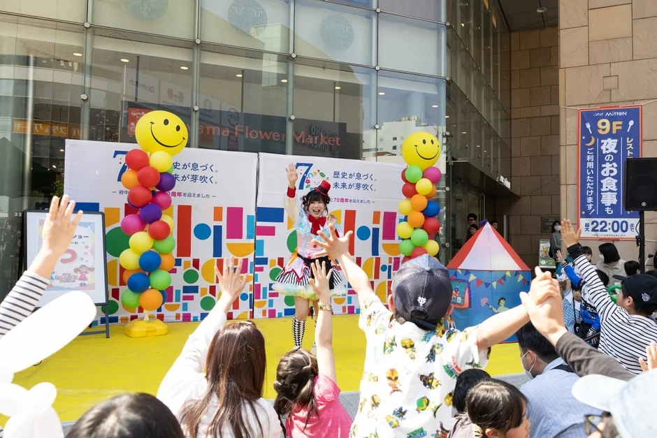 カラフルな衣装のパフォーマーがステージで観客に手を振っている様子