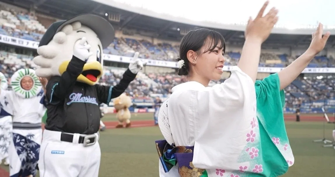 野球場のフィールドで観客に手を振る浴衣姿の女性とマスコットキャラクター