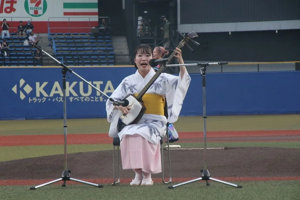 野球場のグラウンドで三味線を演奏する浴衣姿の女性