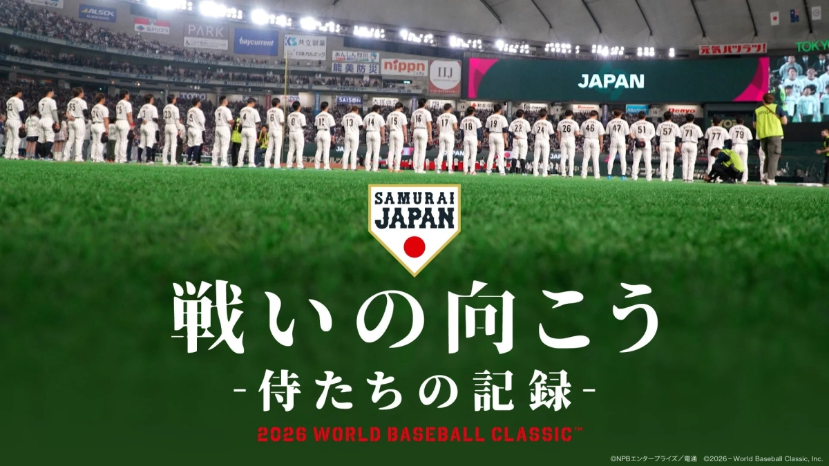 侍ジャパンの選手たちが野球場のグラウンドに整列している様子を捉えた画像です。背景には巨大なスクリーンに「JAPAN」の文字とスポンサーロゴ、そして観客席が見えます。手前には「SAMURAI JAPAN」のロゴと「戦いの向こう -侍たちの記録- 2026 WORLD BASEBALL CLASSIC™」の文字が大きく表示されており、WBCのプロモーション画像であることがわかります。