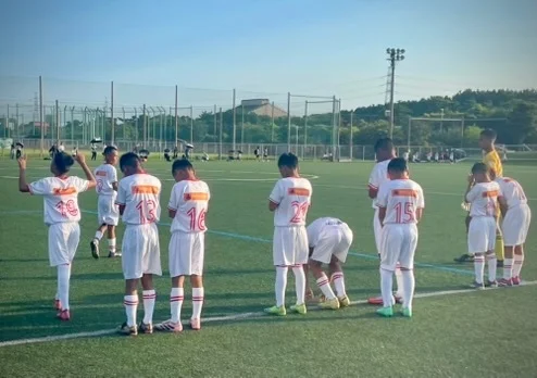 人工芝のサッカーグラウンドで白いユニフォームを着た少年たちが集まっている